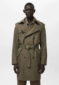 Abrigo tipo trench verde oliva con cierre doble abotonadura, detalle de cinturón y solapas grandes. Hecho de un tejido liso con hombreras y bolsillos.