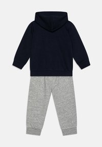 Sudadera con capucha de color navy y mangas largas combinada con pantalones de chándal de color gris claro. Ambos confeccionados en un tejido suave, con puños y cintura elásticos.