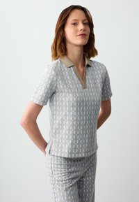 Grijze gemusterde top met een beige kraag, met een diamantpatroon in lichtblauw en goud. Korte mouwen en een relaxte pasvorm, gecombineerd met bijpassende broek.