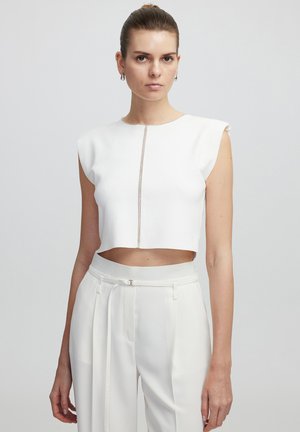 Top bianco corto con maniche a cappuccio, caratterizzato da una cucitura decorativa centrale. Abbinato a pantaloni bianchi a vita alta, in tessuto morbido, e una cintura.