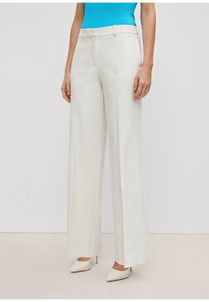 Vrouw draagt witte wijde broek met hoge taille, gecombineerd met witte pumps met spitse neus en een ingestopt felblauw mouwloos topje.