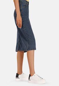 Gonna midi in denim blu scuro, con un taglio classico, tasche laterali e un orlo che arriva sotto al ginocchio. Abbinata a sneaker bianche.