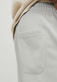 Pantalones de chándal de color gris claro con una textura suave, cintura elástica y un bolsillo trasero que presenta bordes cosidos de manera ordenada.