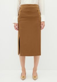 Bruine kokerrok met een zijsplit, een gladde textuur en twee voorzakken. Gepaard met beige schoenen met decoratieve accenten.