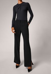 Top negro de manga larga y ajustado con detalle retorcido en el escote, combinado con pantalones negros de cintura alta que presentan aberturas en los laterales del dobladillo.