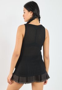 Black ribbed tank top with a round neckline, paired with a dark denim mini skirt featuring a frayed hem and pleated design.