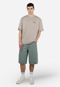 Beige bomull t-skjorte med korte ermer, blå denimshorts og hvite sneakers. Avslappet passform, med subtil logo detalj på t-skjorten.