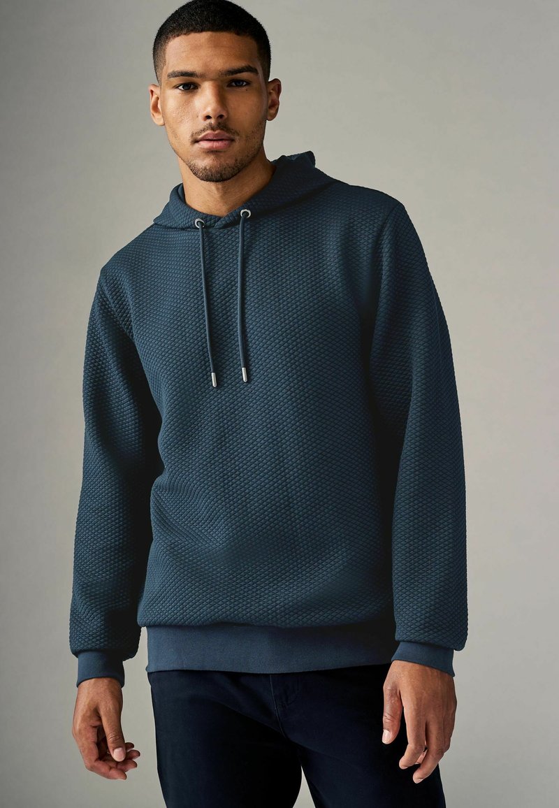 Sudadera con capucha texturizada de color azul oscuro, con cordones y terminales plateados. Puños y bajo acanalados, con un patrón de diamantes en toda la prenda.