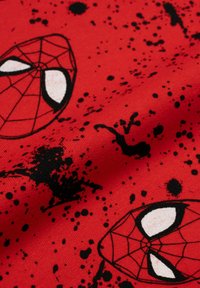 Tessuto rosso con schizzi di vernice nera e due maschere di Spider-Man con contorni neri e occhi bianchi su una superficie testurizzata.