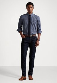 Marineblauw geruit overhemd met knopen, donkere spijkerbroek, bruine riem en bruine loafers. Het overhemd heeft een kraag en de outfit heeft een klassieke pasvorm.