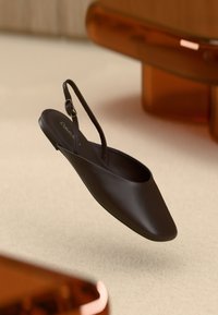 Černá slingback obuv s zaoblenou špičkou a hladkým matným povrchem. Obsahuje štíhlý nastavitelný pásek a plochou podrážku.