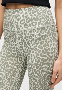 Κολάν μέσης σε απαλή πράσινη απόχρωση με μοτίβο λεοπάρδαλης, κατασκευασμένο από μαλακό υλικό. Διαθέτει διακριτικό λογότυπο στη ζώνη της μέσης.