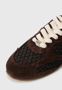 Sneaker in suede marrone e mesh nero con lacci crema, pannello laterale testurizzato e logo metallico sull'etichetta.