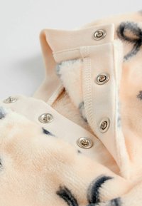 Pfirsichfarbene Fleece-Oberbekleidung mit grauen Mustern. Verfügt über einen Druckknopfverschluss und eine weiche Textur. Kragen-Design in der Ecke sichtbar.