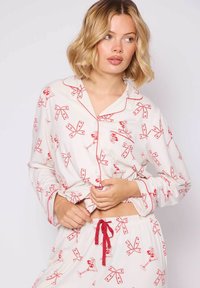 Witte pyjama-set met rode strik en cocktails glas prints. Bevat een knoopsluiting bovenstuk met kraag en rode bies, en een broek met elastische taille.