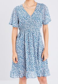 Robe fleurie en bleu et blanc, dotée d'un col en V, de manches courtes, d'un smock à la taille et d'un ourlet à volants. Confectionnée dans un tissu léger.