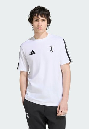 Ung mand med krøllet hår iført en hvid Juventus fodbold t-shirt og sorte bukser med Juventus-logoer på en lys baggrund.