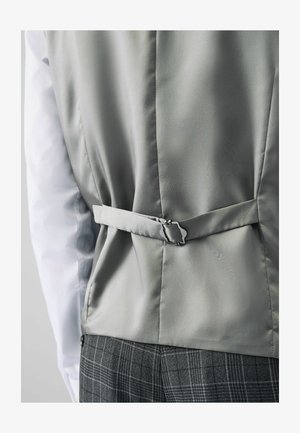 Graue Satinweste mit tailliertem Design, ausgestattet mit einem Rückenverschluss und einer glatten Textur, kombiniert mit einem weißen Hemd und gemusterten Hosen.