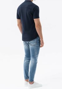Camisa polo de manga corta en color marino con un diseño elegante, combinada con unos jeans de mezclilla azul claro y zapatillas blancas. Tejido suave y silueta ajustada.