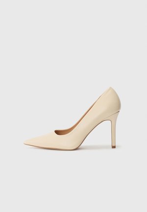 Escarpin en cuir beige à talon haut avec un bout pointu et un détail découpé sur le côté, possédant un talon stiletto fin pour le soutien.