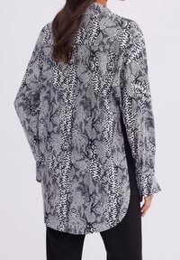 Black and white patterned shirt featuring an abstract design, long sleeves, and a curved hem. Made from lightweight fabric with a smooth texture.