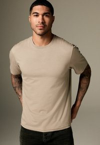 Beige kortærmet t-shirt lavet af blød bomuld, med rund hals og afslappet pasform. Enkelt design uden synlige mønstre eller detaljer.