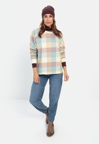 Langærmet, flerfarvet ternet skjorte i pastelfarver med brune manchetter, parret med blå denimbukser og brune ankelstøvler. Mørk hue bæres.