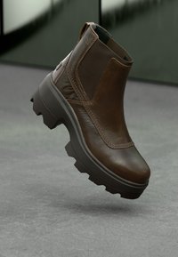 Brune lærankelstøvle med en tyk sål, rund tå og elastiske sidepaneler. Textureret overdel med kontrasterende syninger.