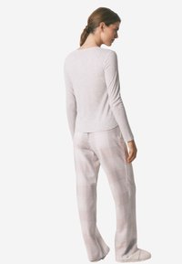 Lichtgrijze gebreide trui met lange mouwen, gecombineerd met licht geruite broek. De trui heeft een ronde achterkant; de broek heeft een comfortabele pasvorm met zichtbaar ruitpatroon.