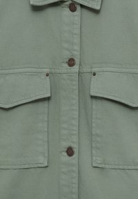 Light green denim shirt with two front pockets, brown snap buttons, and a collared neckline. Textured fabric with visible stitching details.