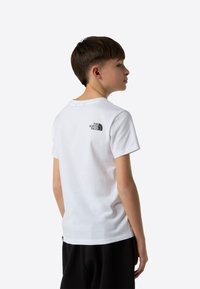 Biały bawełniany t-shirt z okrągłym dekoltem i krótkimi rękawami, z czarnym logo "The North Face" na górnej części pleców.