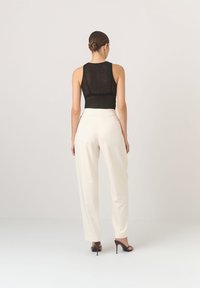 Czarny siatkowy top na ramiączkach w połączeniu z białymi, dopasowanymi spodniami. Szpilki w odcieniu brązowym. Prosta sylwetka z gładką teksturą i czystymi liniami.