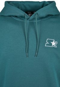 Sudadera con capucha color azul verdoso hecha de material suave, con capucha ajustable con cordón, logo bordado con una estrella y puños acanalados. Textura lisa.