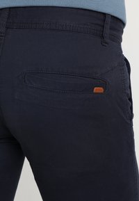 Pantaloni di cotone blu navy con tasca posteriore con dettagli cuciti e una piccola etichetta in pelle marrone con il logo "EDC BRAND".