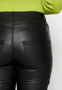 Pantalones de cuero sintético negros con una textura suave, cintura alta y bolsillos traseros. Presenta costuras detalladas y una forma ajustada.