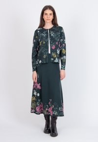 Knitted, dark green two-piece outfit featuring floral patterns in pink, white, and yellow. The top has a round neck and short sleeves, paired with a long skirt.