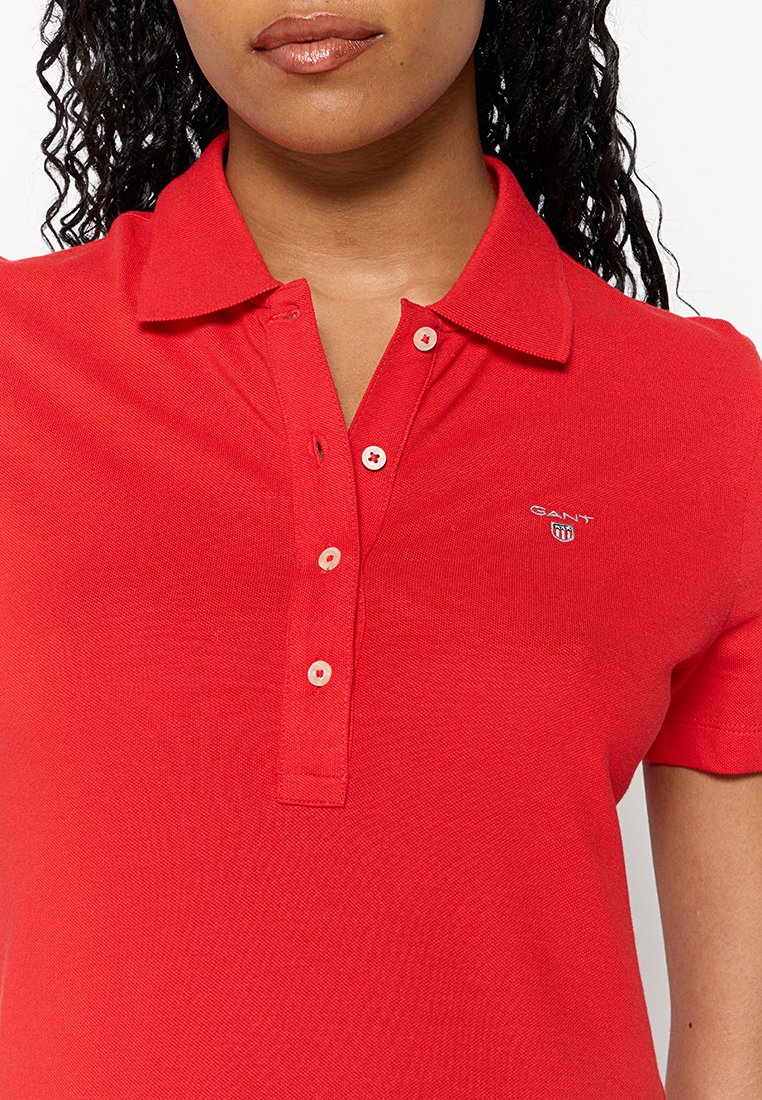 Camisa polo roja confeccionada en tejido texturizado. Presenta un cuello clásico, una tapeta de botones con botones de tono claro y un pequeño logo en el pecho.