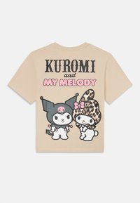 Beige t-paita, jossa on sarjakuvahahmot Kuromi ja My Melody, mustia ja vaaleanpunaisia yksityiskohtia, leopardikuvioinen hattu ja rohkeaa tekstiä.