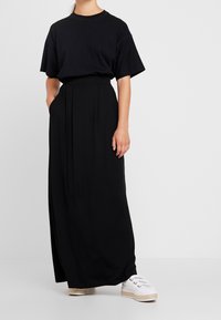 Black oversized t-shirt paired with a long, flowing black maxi skirt. Model wears white sneakers with textured sole.