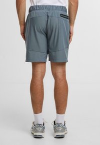 Pánské sportovní šortky v světlé šedé barvě, vyrobené z elastického materiálu, s elastickým páskem a bočními zipovými kapsami. Hladká textura, úzký střih.