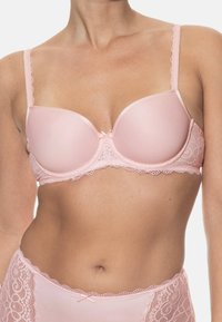 Jasnoróżowy biustonosz z wkładkami i koronkowym wykończeniem, z regulowanymi ramiączkami oraz małą kokardką na środku.
