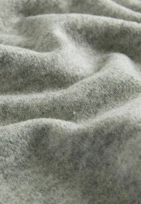 Tekstūruotas pilkas audinys su švelnia, pūkuota paviršiumi. Subtilūs spalvų pasikeitimai sukuria švelnią struktūrą. Medžiaga atrodo šilta ir kviečianti.