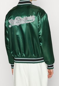 Grüne satinierte Bomberjacke mit gestreiften Rippbündchen und Saum. Verfügt über das weiß gestickte "Huf Worldwide"-Logo auf der Rückseite. Glatte Textur.