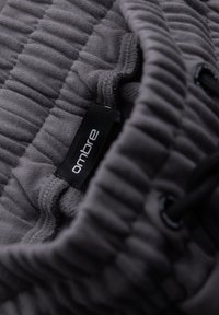 Tissu gris à rayures avec une texture froncée, comportant une étiquette noire sur laquelle est inscrit "ombre". Comprend des cordons de serrage noirs pour réglage.