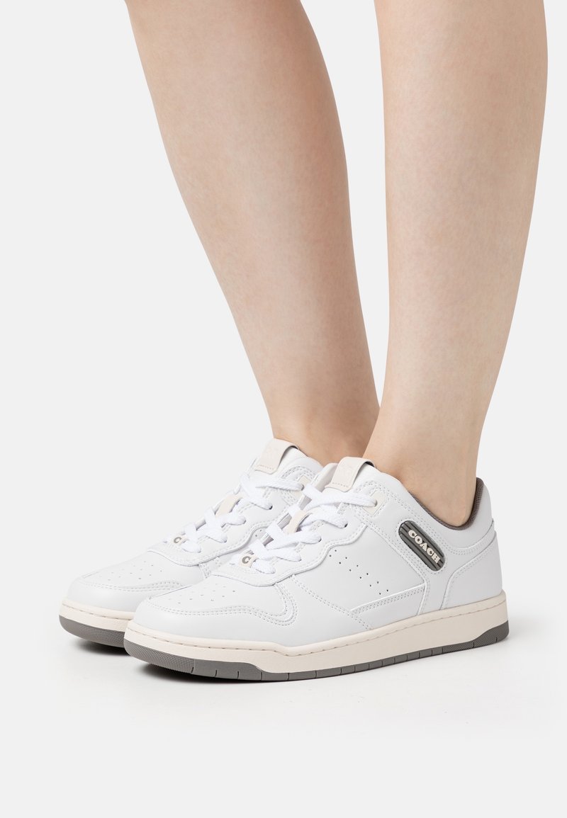 Vita sneakers med läderöverdel, snörningsdesign, perforerad tå, grå accenter och gummisula. Logotyp på sidan nära hälen.