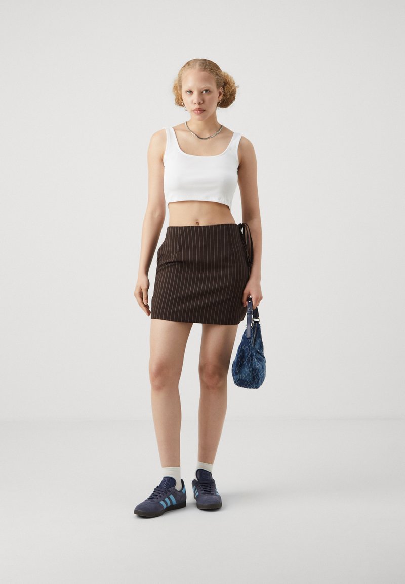 Hvit croppet tanktop, brun pinstriped mini skjørt med sidetau, blå teksturert veske, og mørk blå sneakers med lyseblå striper.