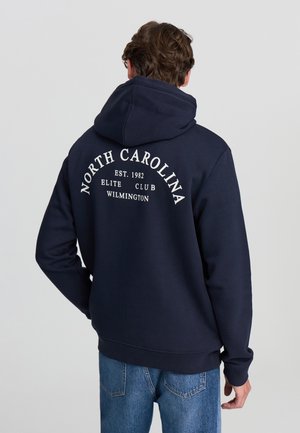 Felpa blu navy con cappuccio e coulisse, con una grande stampa bianca sul retro che riporta "NORTH CAROLINA EST. 1982 ELITE CLUB WILMINGTON."