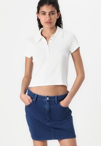 Vit kortärmad polo skjorta med krage och knapprand, kombinerad med en mörkblå denimkjol med framfickor och en figurnära design.