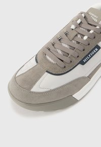 Gray suede sneaker with white nylon accents, rounded toe, padded tongue, and flat laces. Features branding on the side and a textured sole.