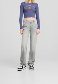 Top corto de manga larga en azul marino con el texto "DINAMARCA" y la bandera. Jeans de pierna ancha en gris claro con cinco bolsillos. Zapatillas negras y blancas completan el conjunto.